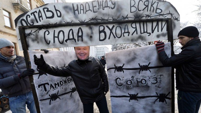 Activist wearing a mask of Ukrainian President Viktor Yanukovych invites passers-by to go through a symbolic gate with the words "Customs Union" and "Abandon hope, all ye who enter here" written on it