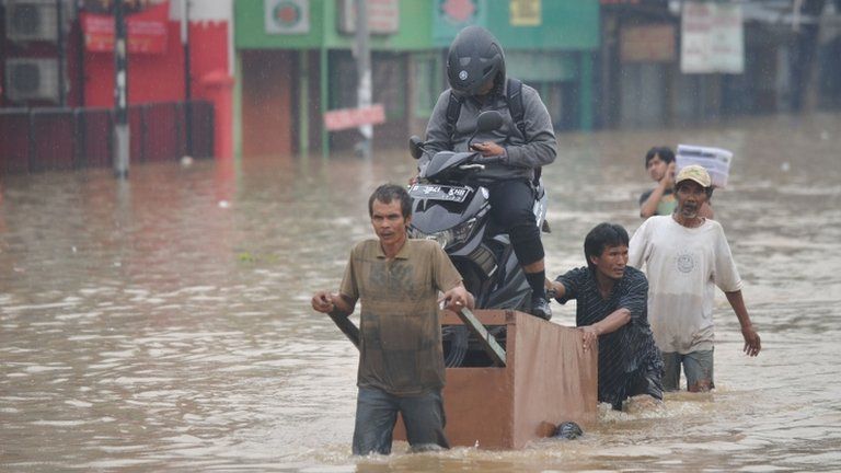 A driver and scooter are transported through floods in Jakarta on 16 January 2013
