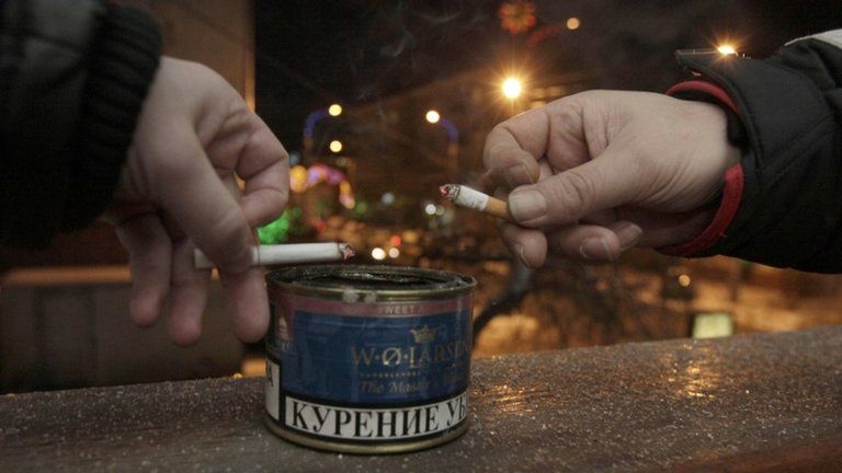 Men drop ash in a tin while smoking on the balcony of an office building in Krasnoyarsk, Russia, 24 January