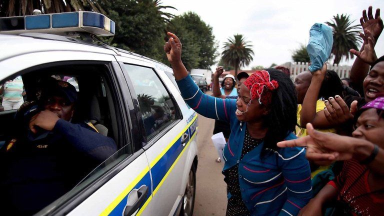 Residents shout at a passing police vehicle as they protest the death of Mozambican taxi driver Mido Macia outside a local police station, in Daveyton, near Johannesburg, South Africa, Friday, March 1, 2013.