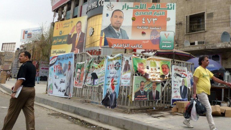 Iraqi men walk past provincial elections campaign poster in Baghdad
