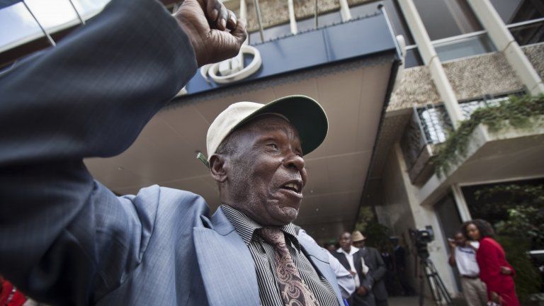 An elderly Mau Mau veteran raises his fist in the air to celebrate as he leaves a press conference announcing a settlement in their legal case for compensation against the British government, in Nairobi, Kenya