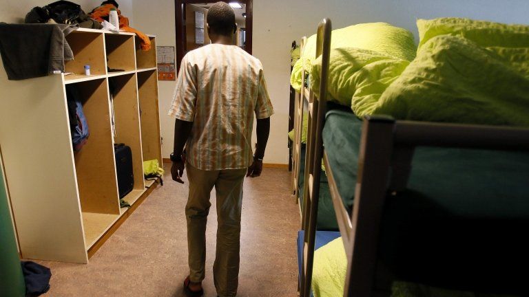 An asylum seeker walks past beds in a sleeping room of the asylum centre "Les Pradieres" for refugees during a tour for media in Val-de-Ruz near Neuchatel