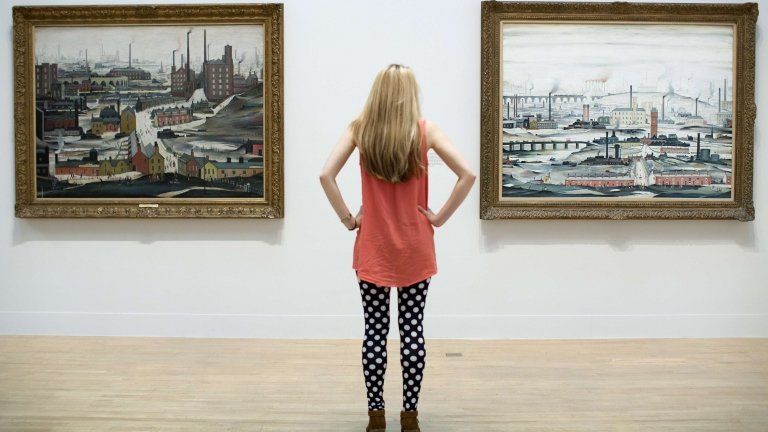 An employee poses for a picture in front of English artist Laurence Stephen Lowry"s paintings "Industrial Landscape (Ashton Under Lyne 1952) (L) and "Industrial Landscape 1955" (R) at the Lowry and the Painting of Modern Life exhibition at Tate Britain in London on June 24, 2013.