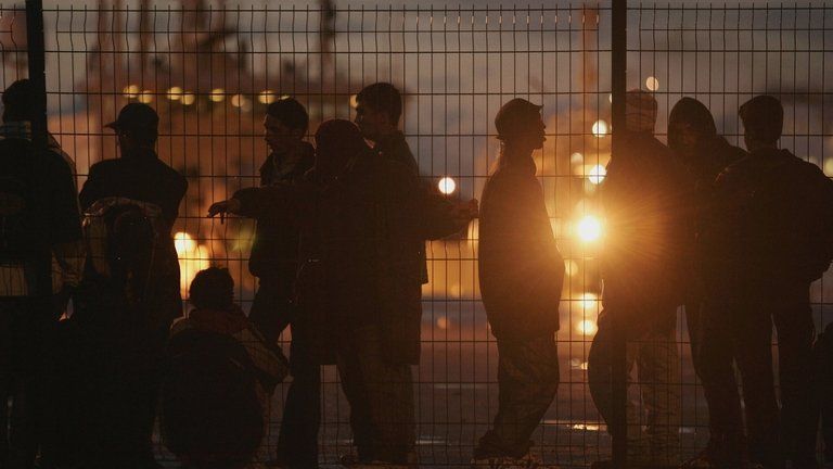 A group of people in shadow at a fence in Calais