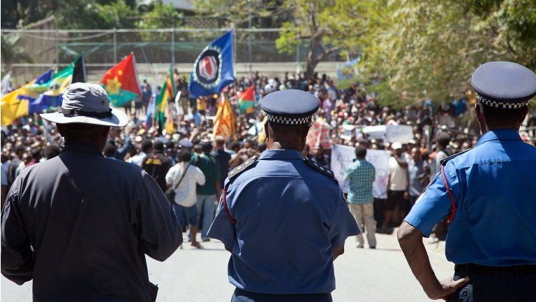 Papua New Guinea police officers watch as hundreds of students march towards the university gate in Port Moresby on 2 August 2013, during a protest rally against Australia and PNG's asylum seeker plan