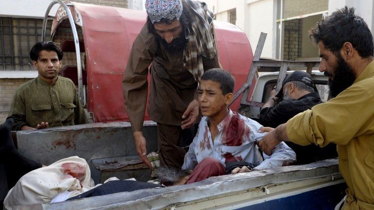 Pakistani bystanders help an injured Muslim youth as he sits in a pickup truck amidst bodies outside a hospital in Quetta on 9 August, 2013, following an attack by gunmen on a mosque.