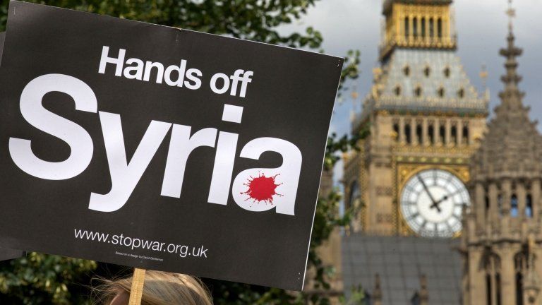 Demonstrators hold up placards during a protest against potential British military involvement in Syria at a gathering outside the Houses of Parliament