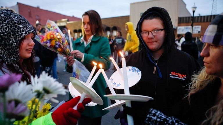 Sarah Linthacum, right, Maggie Baker, second from right, and Gabrielle Stewart, left, try to keep their candles lit despite the wind during the "Justice for Daisy" rally in Maryville, Missouri 22 October 2013