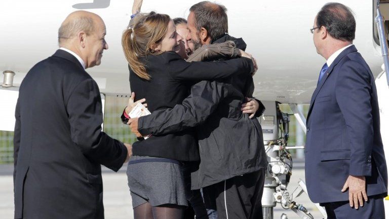 Former French hostage Daniel Larribe is welcomed by relatives as President Francois Hollande (far right) and Defence MInister Jean-Yves Le Drian look on