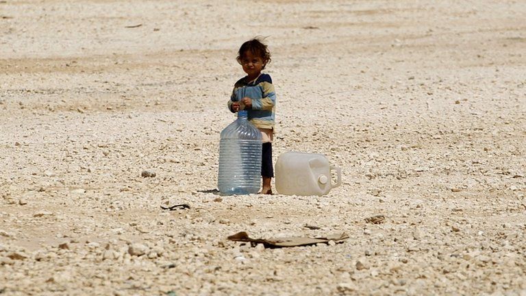A young Syrian refugee stands beside water containers at the Zaatari refugee camp in the Jordanian city of Mafraq