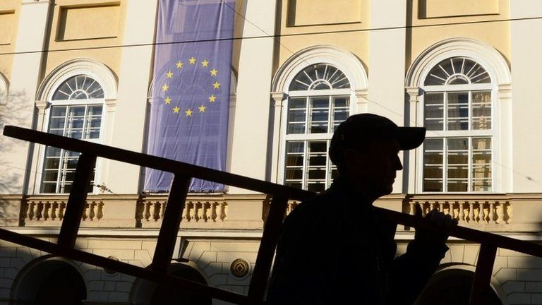 A worker carrying a ladder walks pas an EU flag set on a the city hall of the western Ukrainian city of Lviv