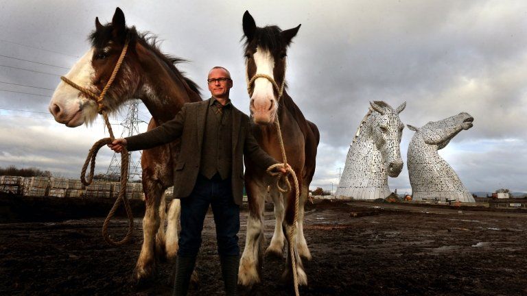 Sculptor Andy Scott stands with two Clydesdale Horses in front of the giant Kelpie heads at Falkirk