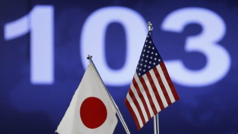 Japanese (L) and American flags are displayed in front of a monitor showing the Japanese yen's exchange rate against the US dollar, in Tokyo, 3 December 2013