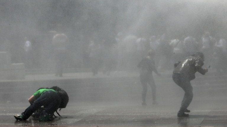 A news cameraman falls to the ground as Turkish riot police spray water cannon at demonstrators in Istanbul, 16 June