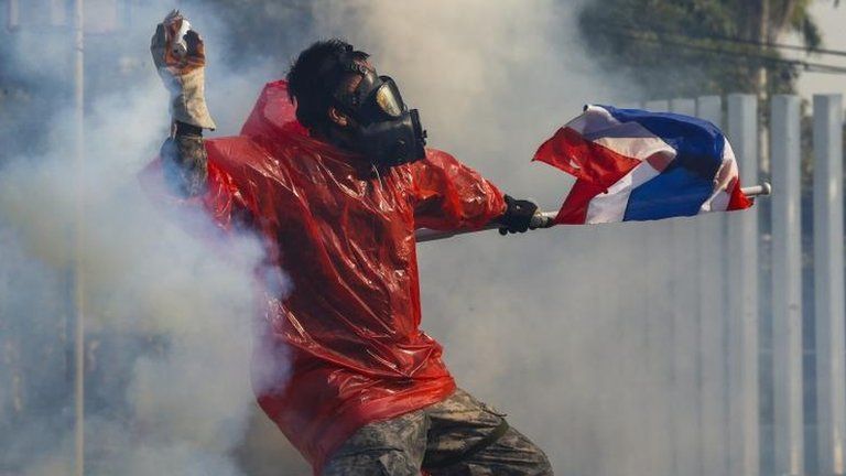 An anti-government protester throws a tear gas canister in central Bangkok, 26 Dec