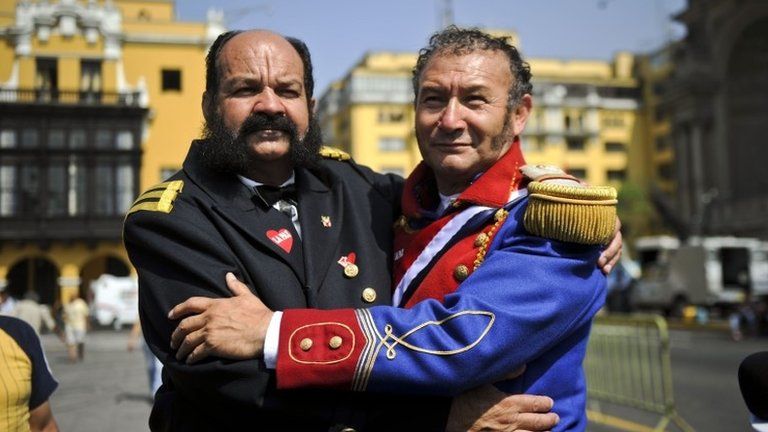 Men dressed as Pacific War heroes from Peru, Miguel Grau (left) and Chile, Bernardo O'Higgins (right) watch on a large screen the reading of the ruling on the maritime dispute between Peru and Chile in front of the government palace in Lima on 27 January, 2014
