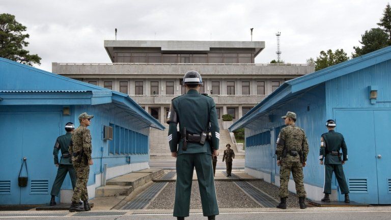 South Korean soldiers look towards the North Korean side as a North Korean solder approaches the UN truce village building that sits on the border of the Demilitarized Zone (DMZ) in Panmunjom, South Korea, on 30 September 2013