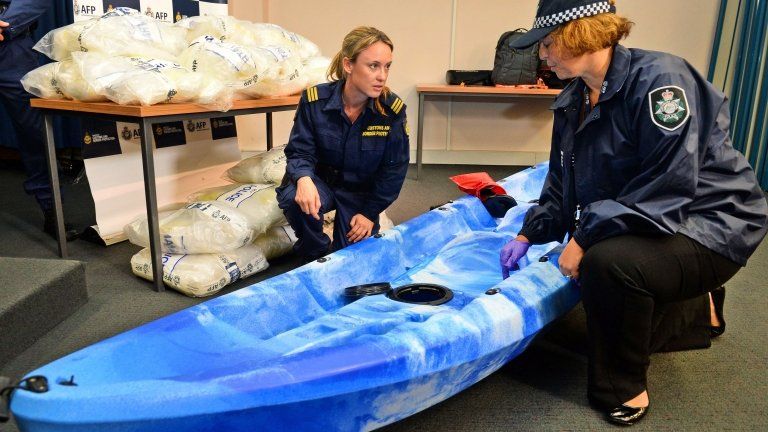 A customs officer (C) and a police officer (R) inspect one of the 27 kayaks seized after Australian authorities found A$180m of methamphetamine stashed in kayaks from China in Sydney on 12 February 2014