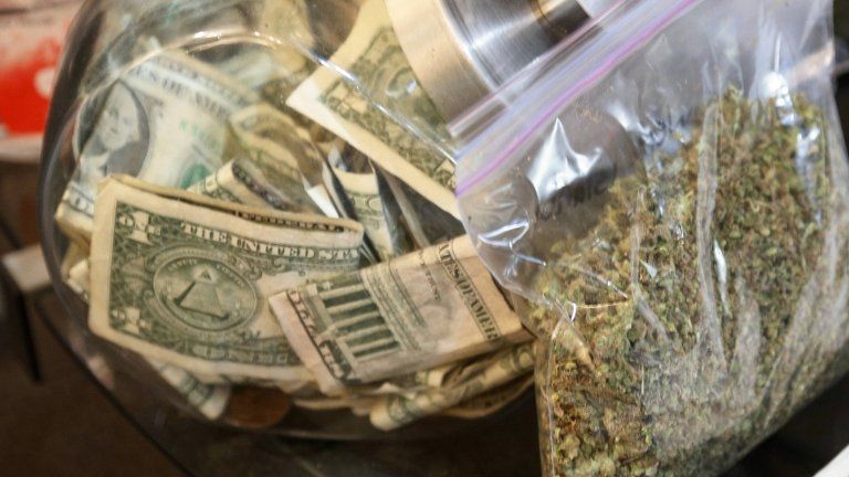 A bag of marijuana being prepared for sale sits next to a money jar in Northglenn, Colorado, on 31 December 2013