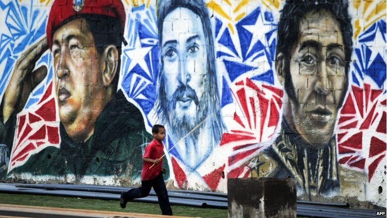 A boy runs next to a mural paint depicting late Venezuelan President Hugo Chavez (left), Jesus (centre) and Latin American Independence Hero Simon Bolivar at 23 de Enero community in Caracas on 4 March, 2014