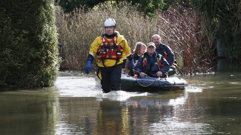 Couple leaving their flooded house in Chertsey by boat