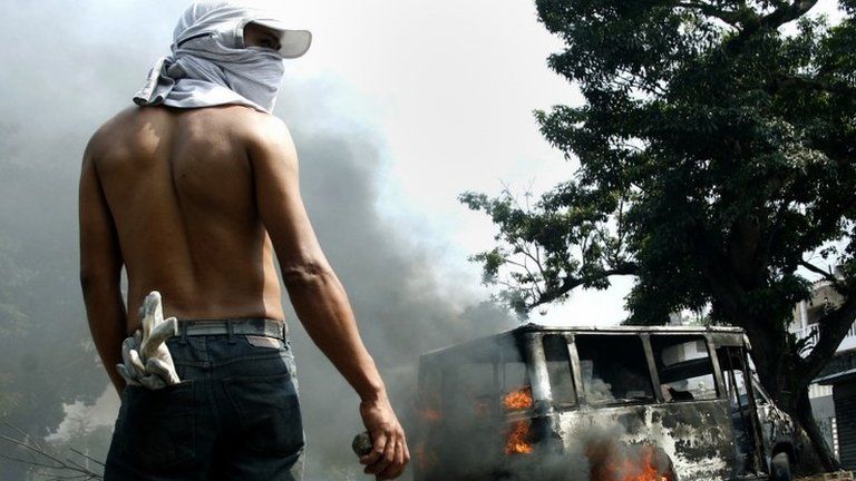 An anti-government protester holds a stone in front of a burning bus during a protest against Nicolas Maduro's government in San Cristobal 17 March, 2014