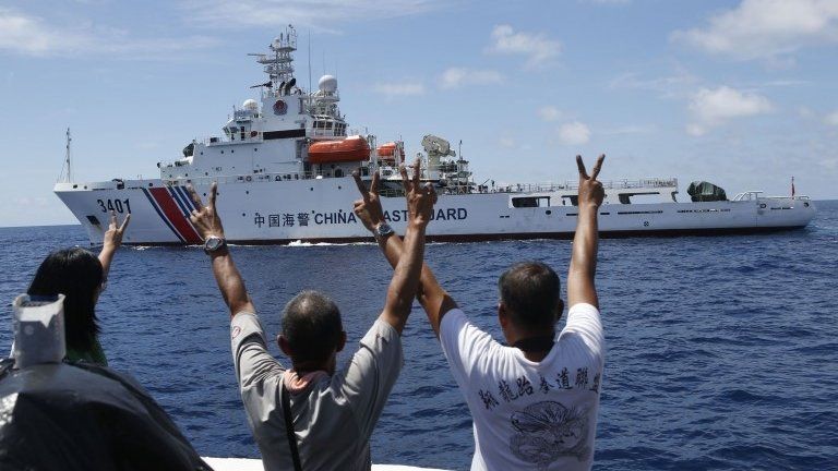 Philippine Marines and a local television reporter (left) gesture towards a Chinese Coast Guard vessel, which twice attempted to block a Philippine government supply ship from reaching the disputed Second Thomas Shoal, part of the Spratly Islands, in the South China Sea, 29 March 2014