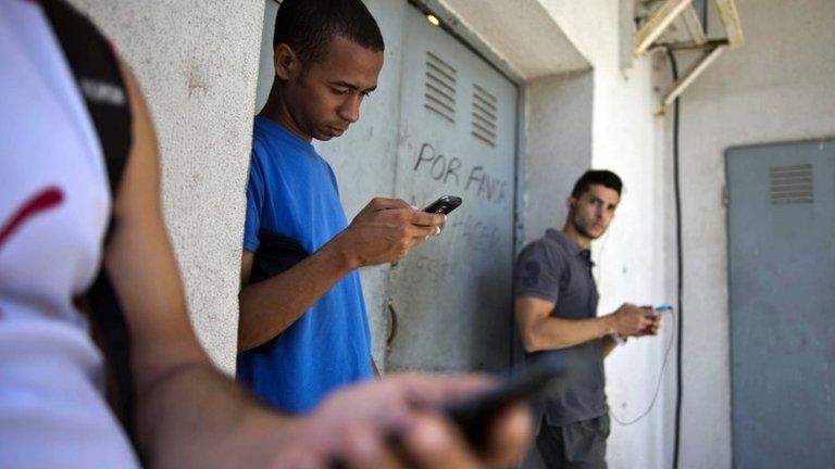 Students gather behind a business looking for a Internet signal for their smart phones in Havana, Cuba, 1 April 2014