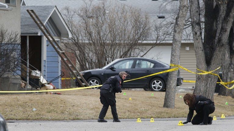 Police officers mark and photograph evidence at a house where five people were stabbed in the early morning hours in Calgary, Alberta on 15 April 2014