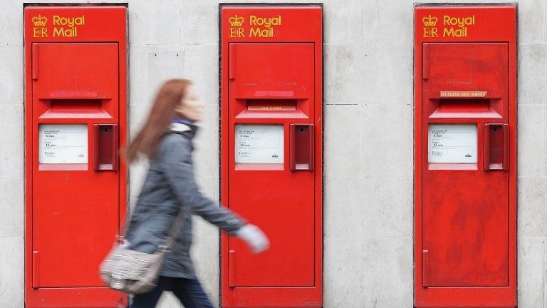 A woman walking past a Royal Mail post office