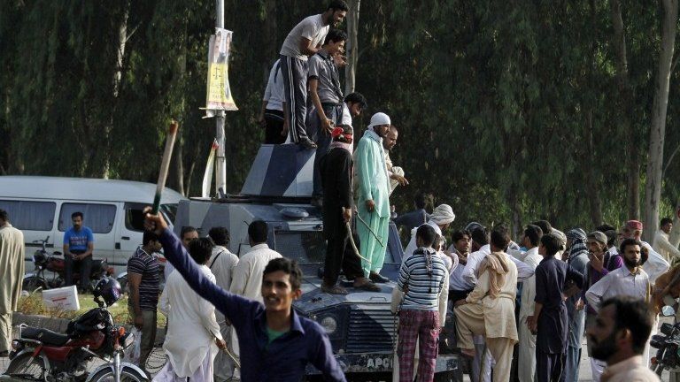 Supporters of Pakistani Muslim cleric Tahirul Qadri, leader of Pakistan Awami Tehreek (PAT) stand on a police armored car after clashing with security forces at Benazir International airport as they gathered to receive their leader in Islamabad, Pakistan, Monday, June 23, 2014.