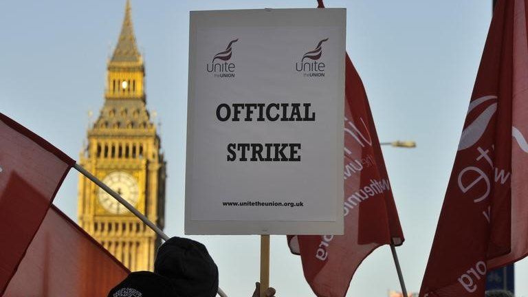 A worker on strike holds a placard saying "Official strike", with Big Ben visible in the background