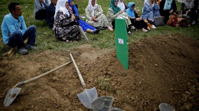Bosnian Muslims sit near a grave after the mass funeral of 175 newly identified victims from the 1995 Srebrenica massacre, in Potocari Memorial Center, near Srebrenica, on 11 July 2014.
