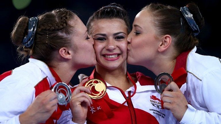 Claudia Fragapane of England is kissed on the podium by Ruby Harrold and Hannah Whelan