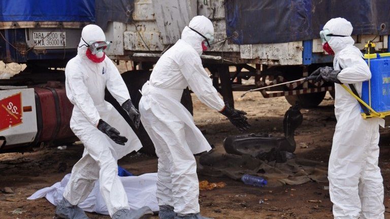 The body of a man, background, suspected of dying from the Ebola virus lies on the ground, as health workers, right, spray themselves with disinfectant, in the capital city of Monrovia, Liberia, 12 August 2014