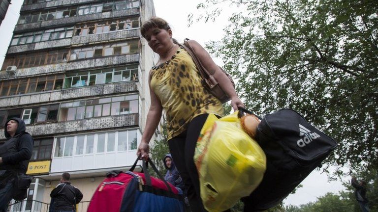 A woman leaves her shell-damaged block of flats in Luhansk, east Ukraine, 8 July
