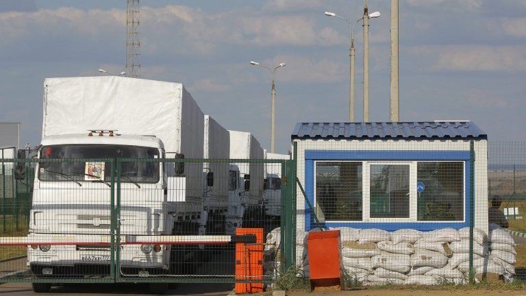 A Russian aid convoy of white trucks waits to enter Ukraine at a border control point
