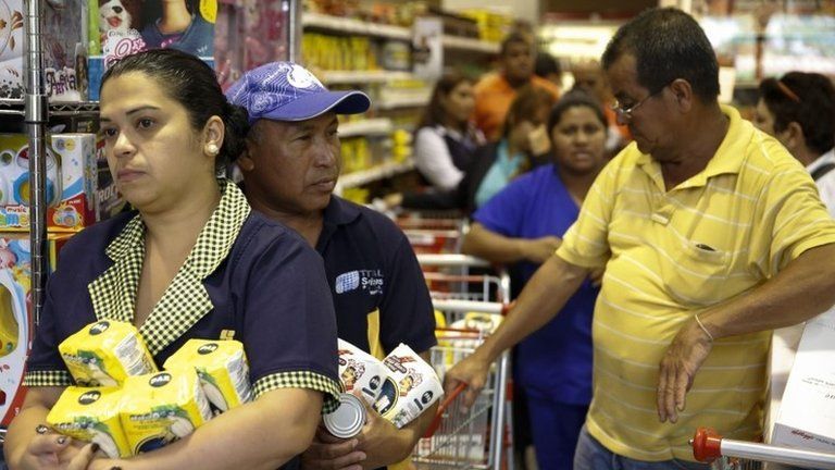 People hold their groceries as they queue to pay the cashier at a supermarket in Caracas on 21 August, 2014.