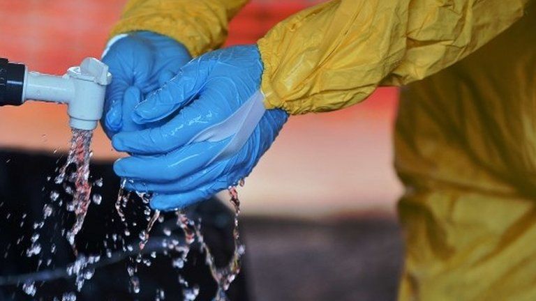 A medical worker in Kailahun, Sierra Leone washes their gloves in chlorine on 15 August 2014.