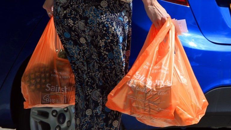 A shopper with Sainsbury's carrier bags