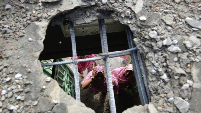 Pakistani villager women are seen through a hole in their house roof caused by a mortar shell allegedly fired across the border at the Dhamala border village near the eastern city of Sialkot in Punjab province