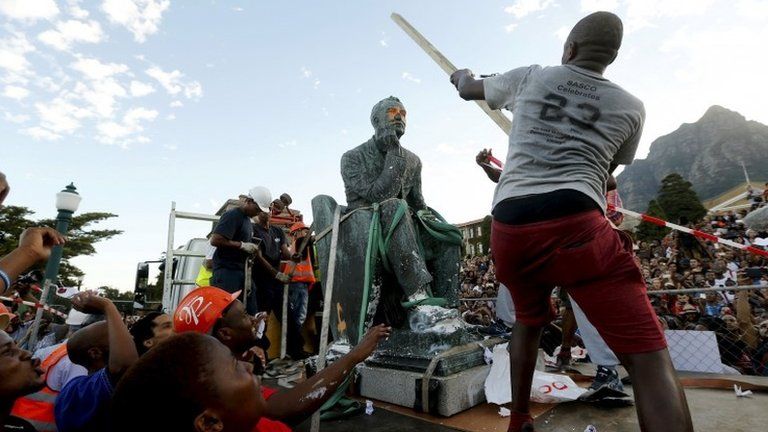A student beats the statue of Cecil John Rhodes with a stick as it is removed from the University of Cape Town (UCT)