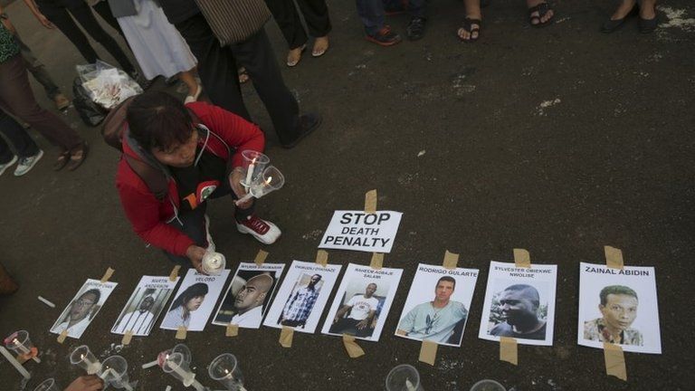 An Indonesian activist holds candles near portraits of the nine inmates