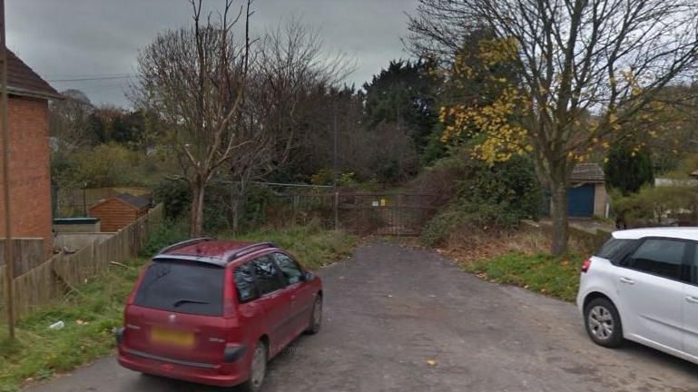 The access to the brownfield site. A red car is parked nearby.