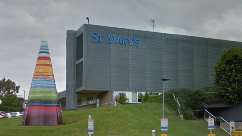 The outside of St Mary's Hospital - a grey building with a sign reading: "St Mary's". A multi-coloured cone sculpture is outside on the grass in front of the building.