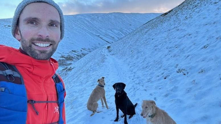 Josh MacAlister on a snowy fell with three dogs