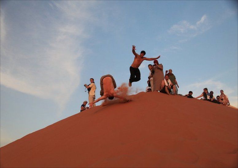 Two men rolling down a sand dune