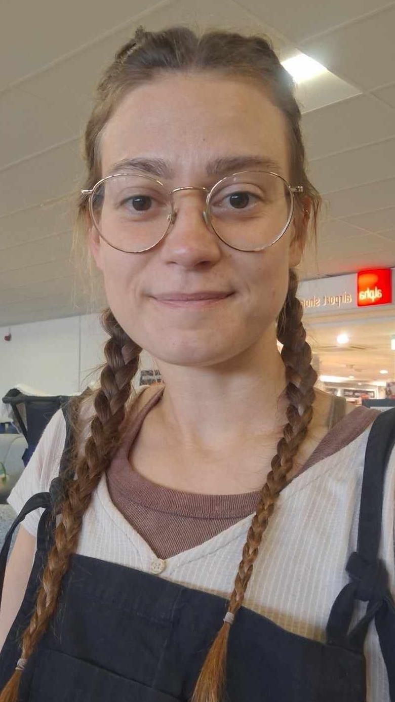 Naomi Wileman is wearing round-metal framed spectacles on her face and her mousey brown hair is in two plaits