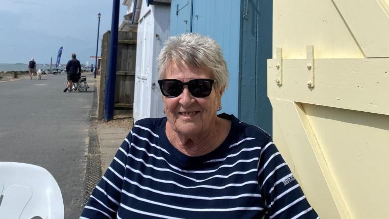 Marian Moules sitting in front of beach huts in Felixstowe.